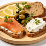 A platter with smoked salmon, cream cheese, and herbs on bread.