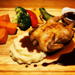 A plate of roasted chicken with mixed vegetables on the side.