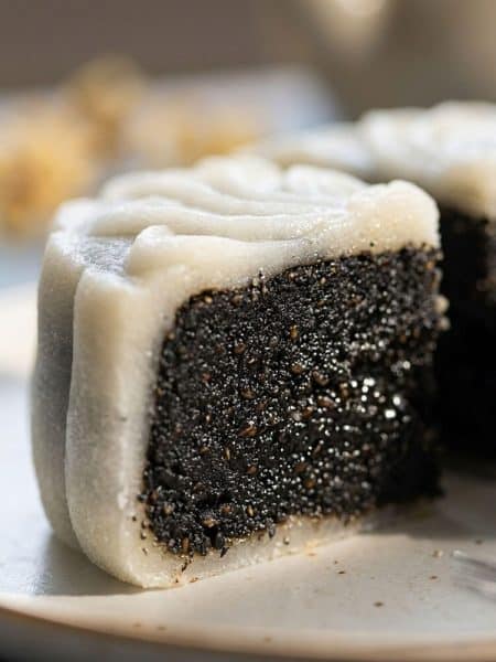 Macro extreme close-up of a cut snow skin mooncake cross-section revealing a dense, glossy black sesame seed paste filling inside a translucent chewy white skin