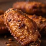 Macro extreme close-up of a steaming hot, golden-brown crispy chicken wing tip crusted with toasted minced garlic bits on a dark wood board