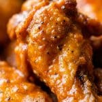 Macro extreme close-up of a glossy, fiery hot buffalo chicken drumette showing blistered crispy skin coated in red-orange pepper sauce and cracked black pepper