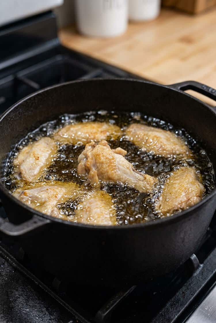 Rested chicken wings frying in a heavy cast iron pot of shimmering hot oil as the skins begin turning golden and crisp