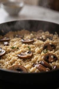 Close-up view of steaming savory long grain rice cooked with plump sliced cremini mushrooms and fresh thyme sprigs in a black skillet