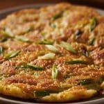 Extreme macro close-up of the crispy golden crust and tender noodlefish interior of Chinese silverfish egg pancake garnished with scallions.