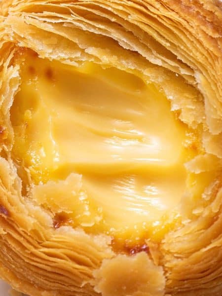 Close up cross section of a flaky egg tart showing paper-thin laminated pastry layers and silky custard center.