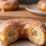 Macro close-up of a broken glazed yeast donut showing an ultra-fluffy, airy crumb with tender open air pockets and a delicate crackled glaze crust
