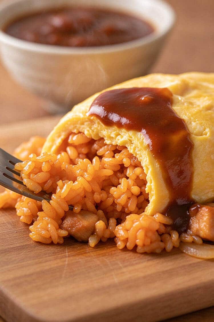 Macro close-up of a metal fork scooping a bite of caramelized ketchup fried rice with tender chicken from inside a soft, barely-set golden egg blanket coated in savory sauce