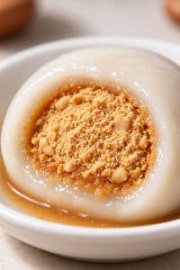 Close up cross section of a chewy peanut tang yuan dumpling showing soft translucent skin and crumbly sweet peanut center.