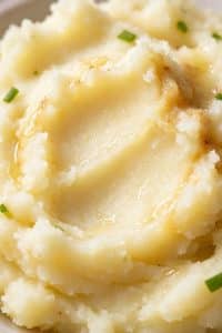 Close up texture of silky smooth mashed potatoes swirling with melted golden butter and fresh chive specks.