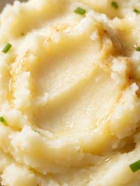 Close up texture of silky smooth mashed potatoes swirling with melted golden butter and fresh chive specks.