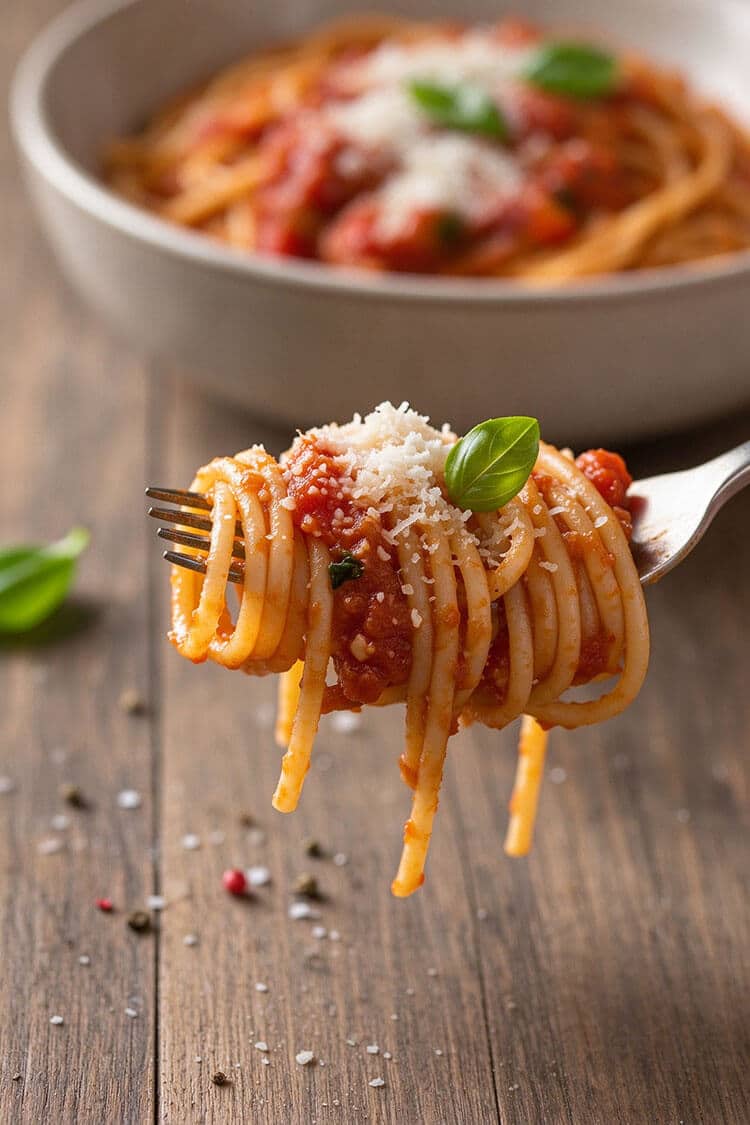 Macro close-up of a fork holding a neat twirl of glossy al dente spaghetti coated in thick tomato sauce, topped with grated Parmesan and a tiny fresh basil leaf