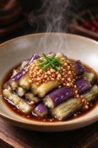 Close-up shot of tender cooked eggplant smothered in glossy minced garlic sauce with steam rising.